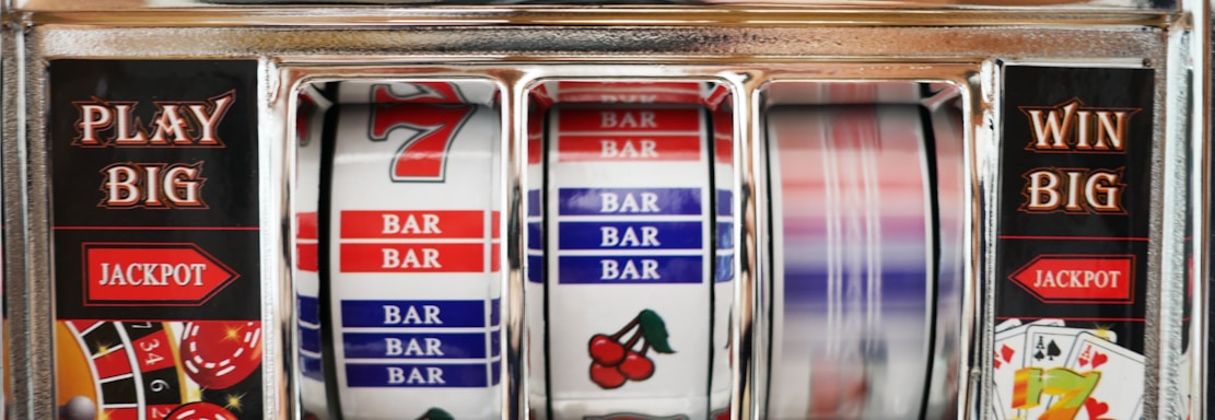 A close-up view of a slot machine with vibrant colors and various gambling symbols such as dice, coins, and playing cards. The reels display a combination of symbols, including bars, cherries, and the number seven. The chrome exterior and colorful details convey the theme of casino and gambling.